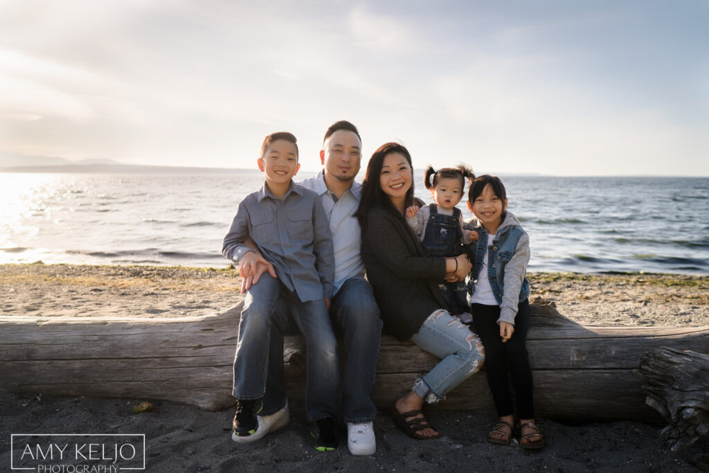Young family sitting on log on beach at Carkeek Park in Seattle