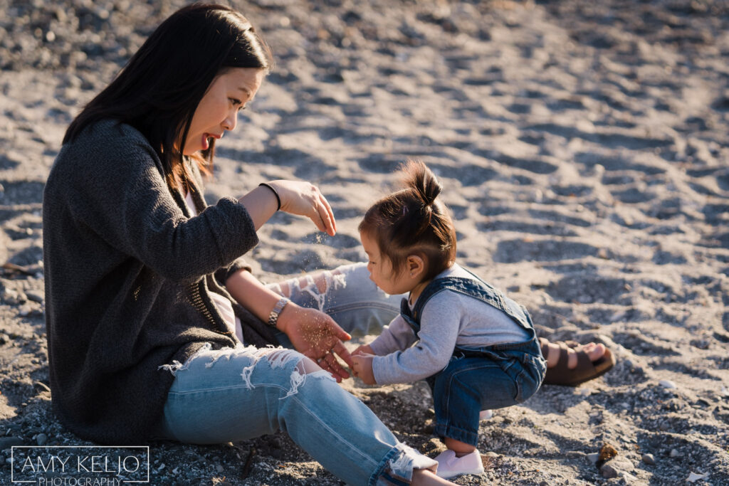 Mother playing in sand with baby daughter on beach at Carkeek Park in Seattle