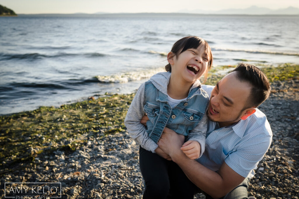 Father tickling his daughter on beach at Carkeek Park in Seattle