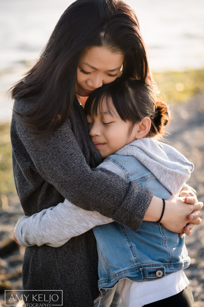 Mother hugging daughter on beach at Carkeek Park in Seattle