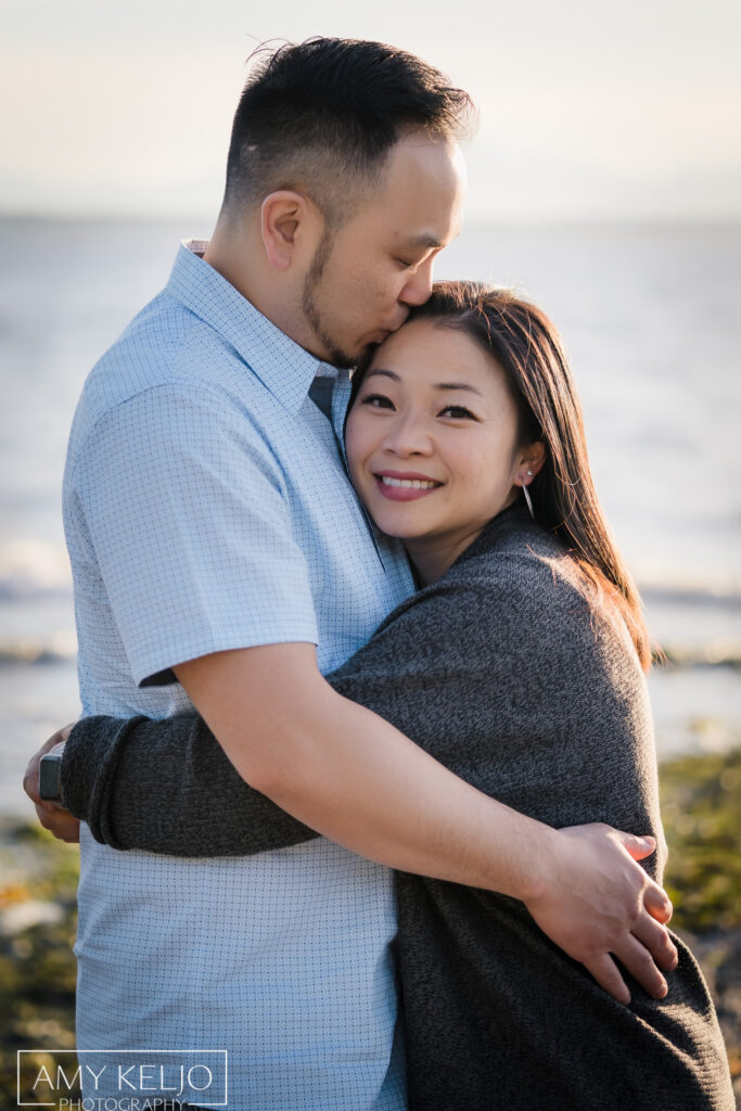 Father kissing mother on beach at Carkeek Park in Seattle