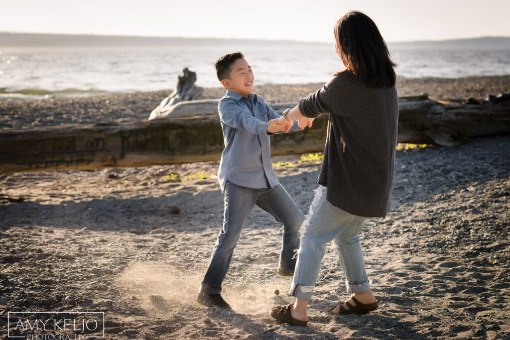 Mother spinning son around on beach at Carkeek Park in Seattle
