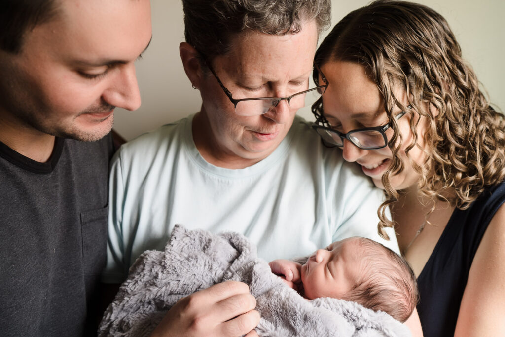 Grandmother and new parents admiring newborn at home photo shoot in Seattle