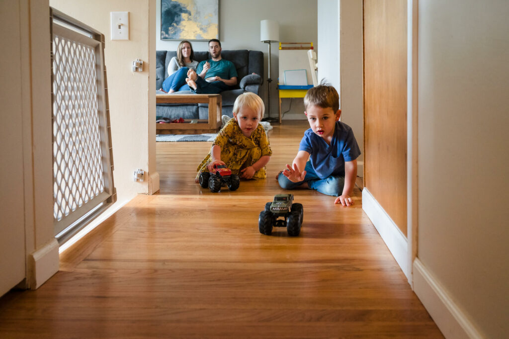 Documentary family photography of young siblings playing with cars while parents watch