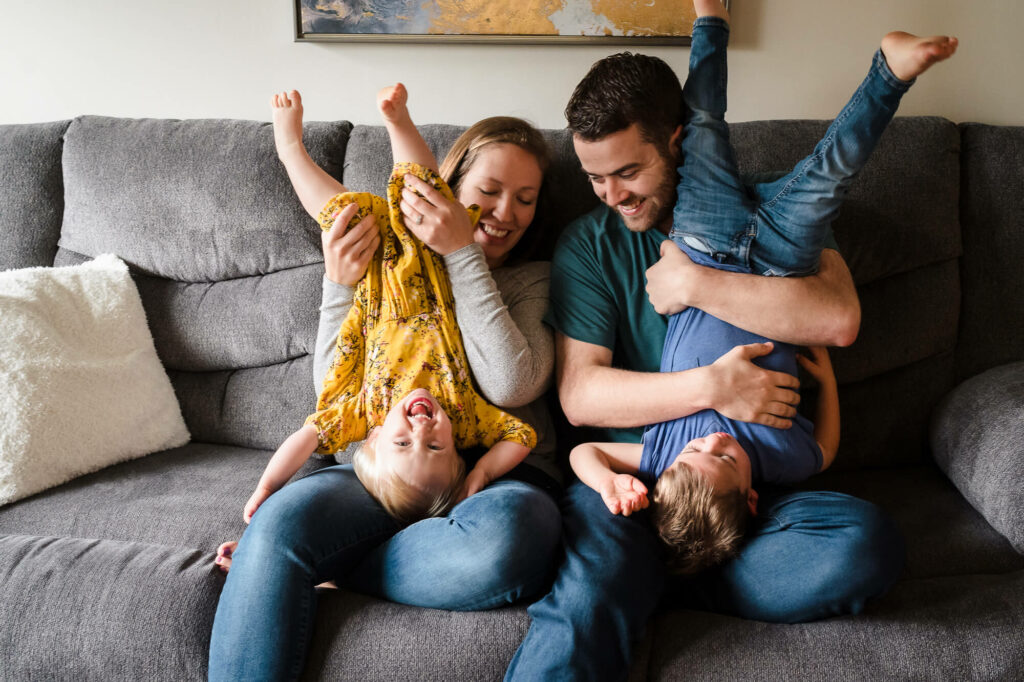 Documentary family photography of parents tickling their son and daughter on the couch in their living room 